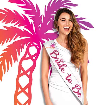 A woman wearing a white 'Bride to Be' sash with an ombre palm tree design in pink, orange, and gold shades.