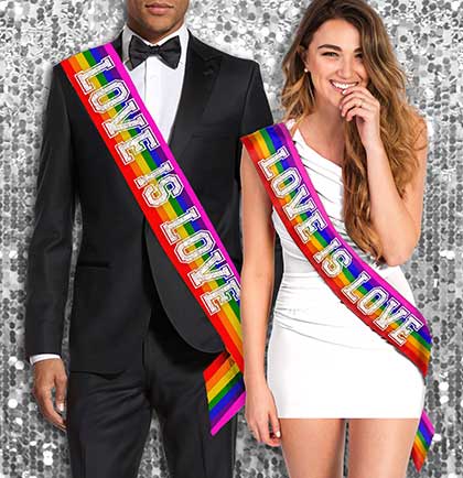 An image showing two adults wearing the 'Love is Love' rainbow sash, one male in a tuxedo and one female in a white dress. The sash has a rainbow color with the text in silver glitter.
