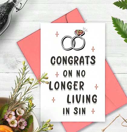 Card with wedding rings and text 'Congrats on no longer living in sin' on a white background with pink envelope and flowers.