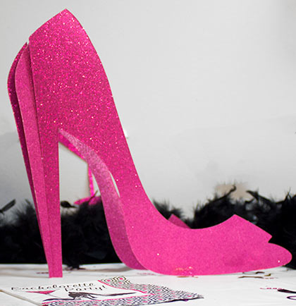 Pink high-heeled shoe with text about giant size and pink sparkle on a white background