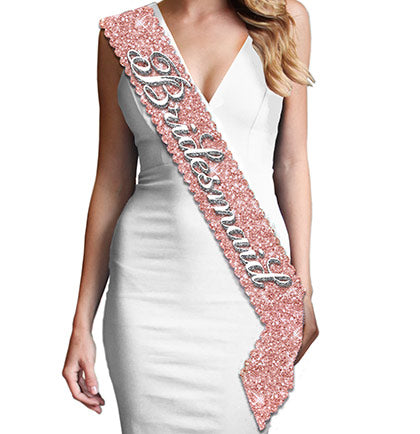 Have all your bridesmaid to match at the bachelorette party or bridal shower. Exclusively at The House of Bachelorette this rose gold sparkle sash says Bridesmaid in a pretty white flirty font. The sash is made with a sparkle fabric that does not shed and has a smooth satin on the backside for a pleasant fit.  